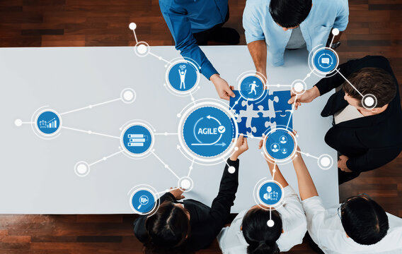 Aerial view of a team working together to solve puzzles representing agile project strategies. Icons depict connections to enhance business solutions and workflow efficiency. Amity