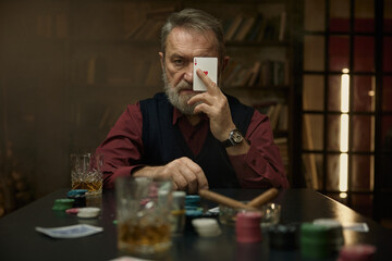 A focused gentleman with a groomed beard holds a playing card