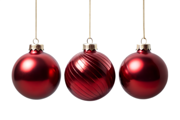 Photo of three shiny red christmas ornaments hang suspended by golden threads, one with a swirling pattern, against a clean transparent background
