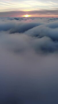 gentle drone video glides over endless, undulating clouds at dawn/dusk, golden sunball casts diffused light and long shadows, revealing intricate cloud textures, with ethereal pastel skies, concept