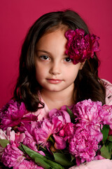 Naklejka premium Young Caucasian girl with flowing dark hair, adorned with flowers, against a vibrant pink backdrop, exuding innocence and beauty.