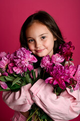 A cheerful girl of Asian descent holds a bouquet of vibrant pink flowers against a bright pink...