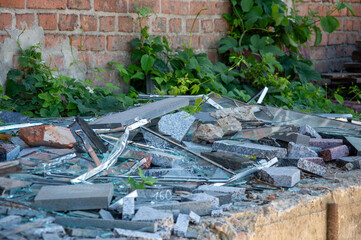 Shattered glass and broken stones are scattered across a neglected area, overtaken by weeds and...