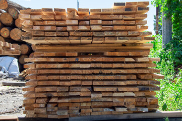 Freshly cut and stacked lumber awaits craftsmanship at a woodworking area under bright sunshine,...