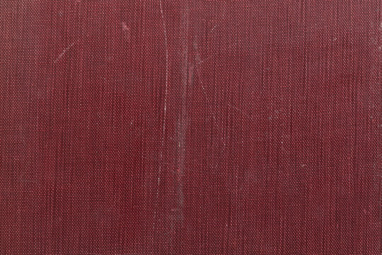 Close-up of worn antique red book cover with heavy texture and signs of age

