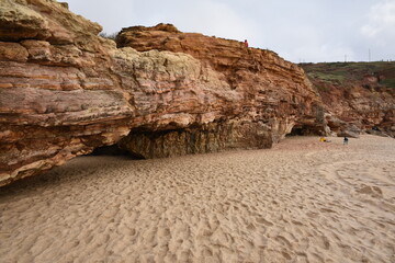 Colorful sandstone cliffs and a sea cave at Praia do Norte, Nazaré, Portugal, with hikers...