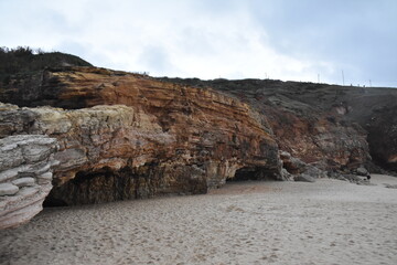 Colorful sandstone cliffs and a sea cave at Praia do Norte, Nazaré, Portugal, with hikers...