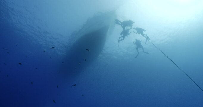 scuba divers fnishing dive doing safety stop on a rope underwater