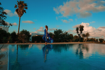 Woman in Flowing Blue Dress by Poolside on Sunny Day
A woman in a vibrant blue maxi dress and...