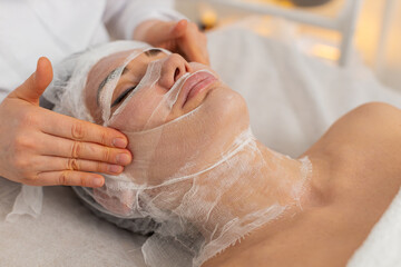 Middle-aged woman begins carboxytherapy treatment in cosmetology clinic. Beautician gently places...
