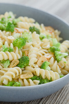 Fusilli or rotini pasta with broccoli, roasted garlic slices, herbs and olive oil, served in blue bowl (Selective Focus, Focus one third into the dish)