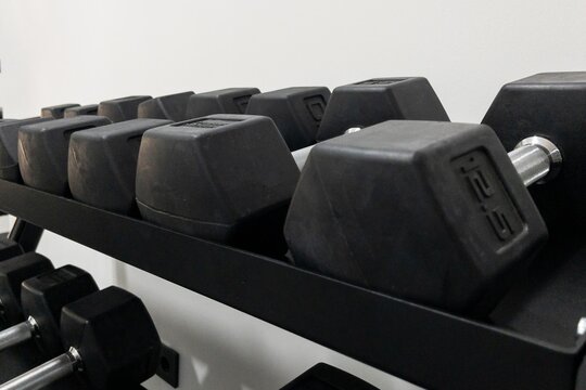 Set of hexagonal dumbbells arranged neatly on a black rack in a modern gym environment