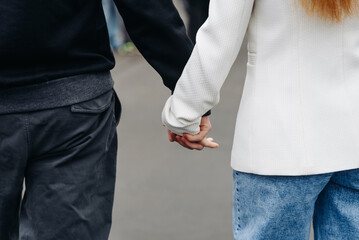 close-up view of couple holding hands, young beautiful caucasian man and woman take each other hands, walking on pathway in park in summer at sunset, love and family concept, selective focus