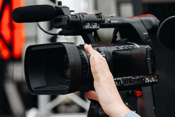 large black video camera on tripod, close-up view, videographer working at music festival in city park, rock group performing on stage