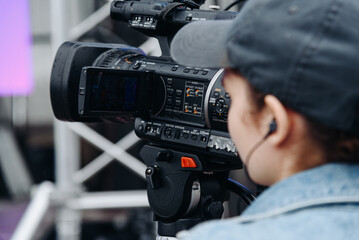 large black video camera on tripod, close-up view, videographer working at music festival in city park, rock group performing on stage