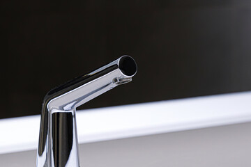 A sleek, touchless chrome tap touchless installed on a contemporary white sink surface. Modern chrome sensor faucet in public washroom
