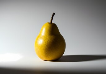 Studio shot of a single yellow pear on a white surface with dramatic lighting creating a strong shadow, perfect for food blogs, healthy eating campaigns, and minimalist designs.