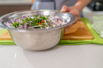 Chef adding spices to peruvian ceviche in a metal bowl
