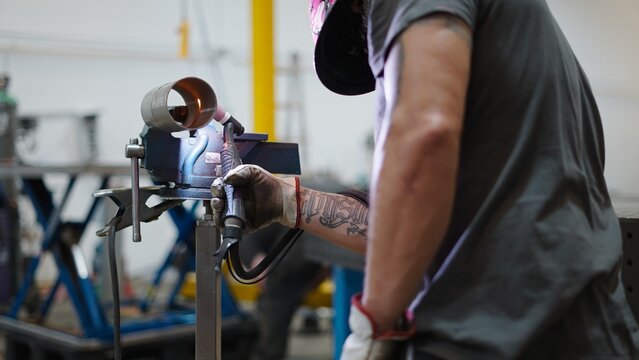 Skilled metal worker joining pipes with welding torch in a metalworking workshop