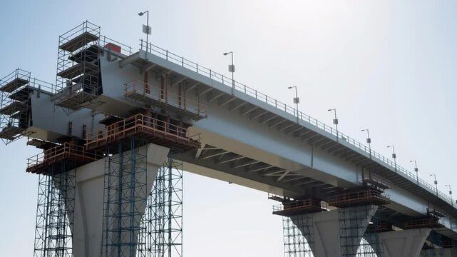 New bridge construction with rising supports and extending span against a bright sky, infrastructure development footage.