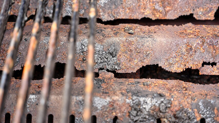Close-up view of a corroded metal surface and rusty grill grates in natural light.