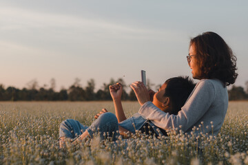 A mother and son enjoy a joyful moment during sunset in a flower field. Capturing the beauty of family love, happiness, and togetherness in nature. Summer, travel, vacation, relaxation. Mother's Day.