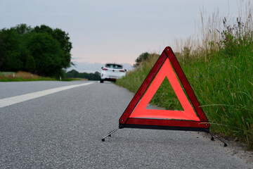 At the side of the road is a warning triangle, behind it a white car with a breakdown