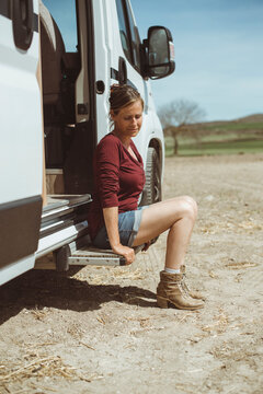 Side view of a woman in denim shorts sitting on the step of a parked camper van