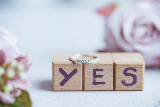 Close-up of a Diamond engagement ring on blocks spelling out the word Yes and roses on a table