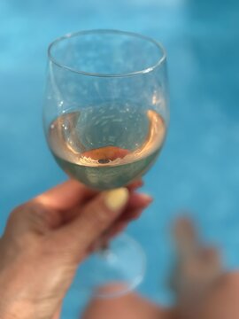Close-up of a woman sitting at the edge of a swimming pool holding a glass of rose wine