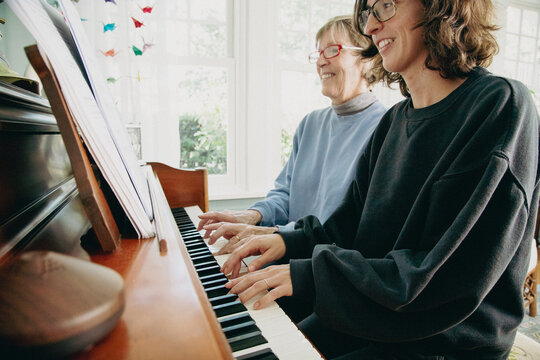 Side view of a smiling mid adult woman and senior woman sitting side by side playing the piano