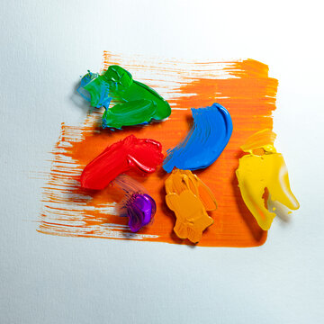 Assorted multi coloured paint blobs on a piece of glass over a brush stroke of red paint