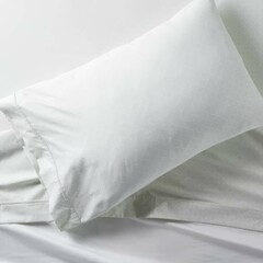 Obraz premium Soft white pillow resting on a neatly arranged bed with light-colored sheets in a serene bedroom setting.