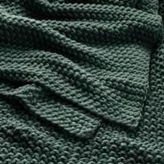 Cozy green knitted blanket draped casually over a soft surface in a warm, inviting setting.