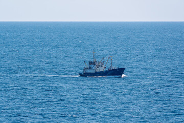 Fishing boat in blue sea and clear sky with birds flying overhead.