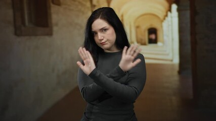 Brunette woman shrugging on university campus corridor with arches and brick walls conveying confusion or uncertainty in an academic setting
