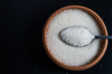 Flat lay of a wooden bowl filled with white sugar and a stainless spoon resting on top