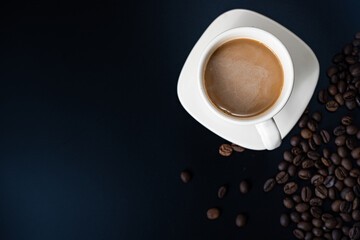 Flat lay of a white cup of coffee with coffee beans on a dark background