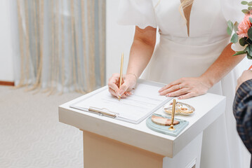 young woman standing at wedding ceremony and signing wedding documents, bride in white dress,, cropped, unrecognizable