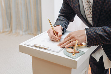 young man standing at wedding ceremony and signing wedding documents, groom in black costume, cropped, unrecognizable