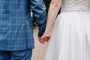 close-up view of couple holding hands, bride and groom, young beautiful caucasian man and woman take each other hands, walking on pathway in park in summer, love and family concept, selective focus