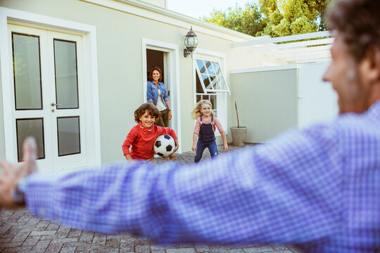 Young father coming home after a long business trip to his family and children welcoming him in the driveway of his home