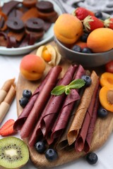Tasty candied leather rolls, fruits and berries on white table, closeup