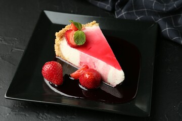 Piece of tasty cheesecake with strawberries, sauce and mint on black table, closeup