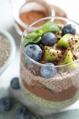 Delicious chocolate pudding with chia seeds, kiwi, mint and blueberries in glass on grey table, closeup