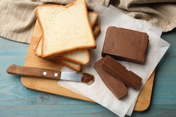 Pieces of tasty chocolate butter, slices of bread and knife on light blue wooden table, top view