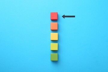 Maximum. Colorful cubes and arrow pointing at red one on light blue background, flat lay