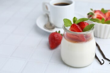 Tasty panna cotta with caramel, strawberries, mint, vanilla pods and coffee on white tiled table, closeup. Space for text