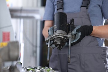 Auto part. Professional mechanic with starter motor indoors, closeup. Space for text