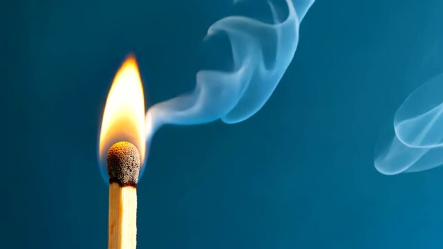 A close-up of a lit matchstick with smoke curling against a blue background, symbolizing ignition